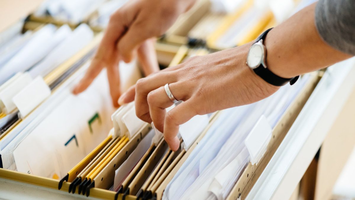 Pair of hands wearing a wedding band and a watch flip through files