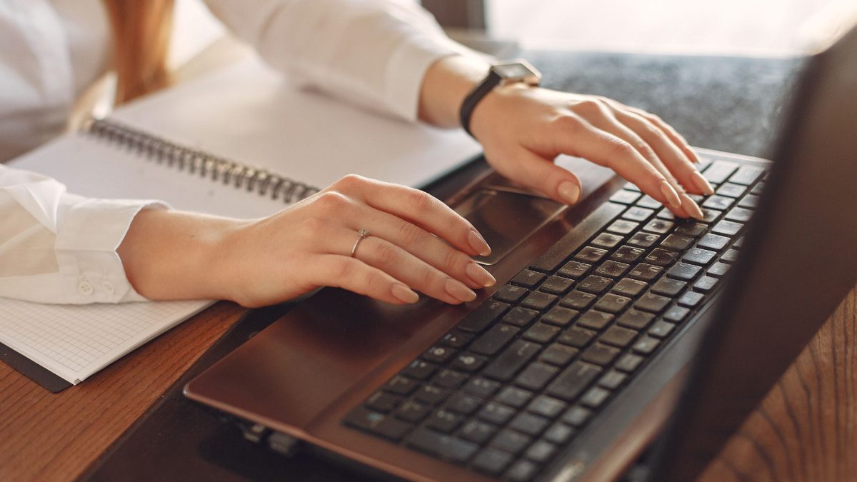 Feminine hands typing at a black keyboard.